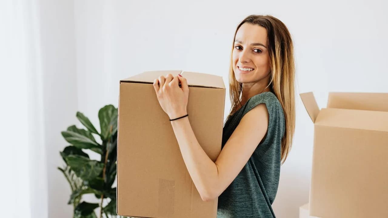 Frau in grünem Hemd trägt einen gepackten Umzugskarton in die neue Wohnung