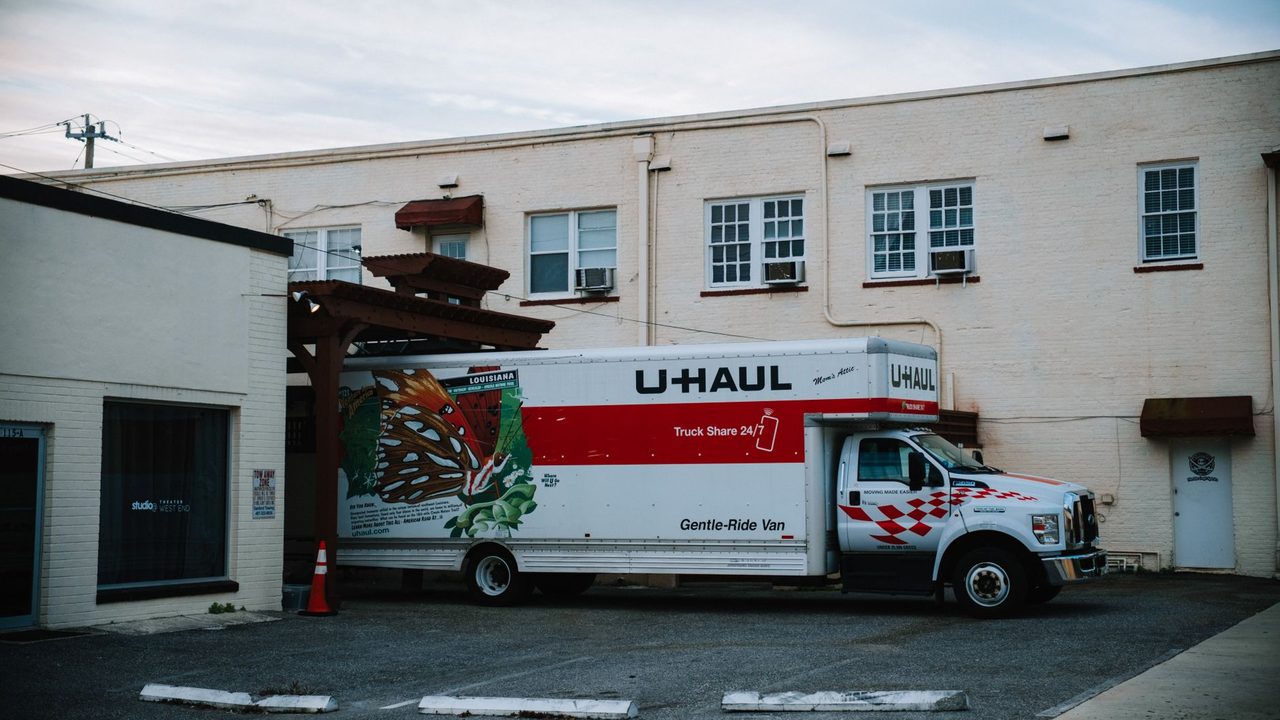 A U-Haul moving truck parked in front of a beige warehouse building.